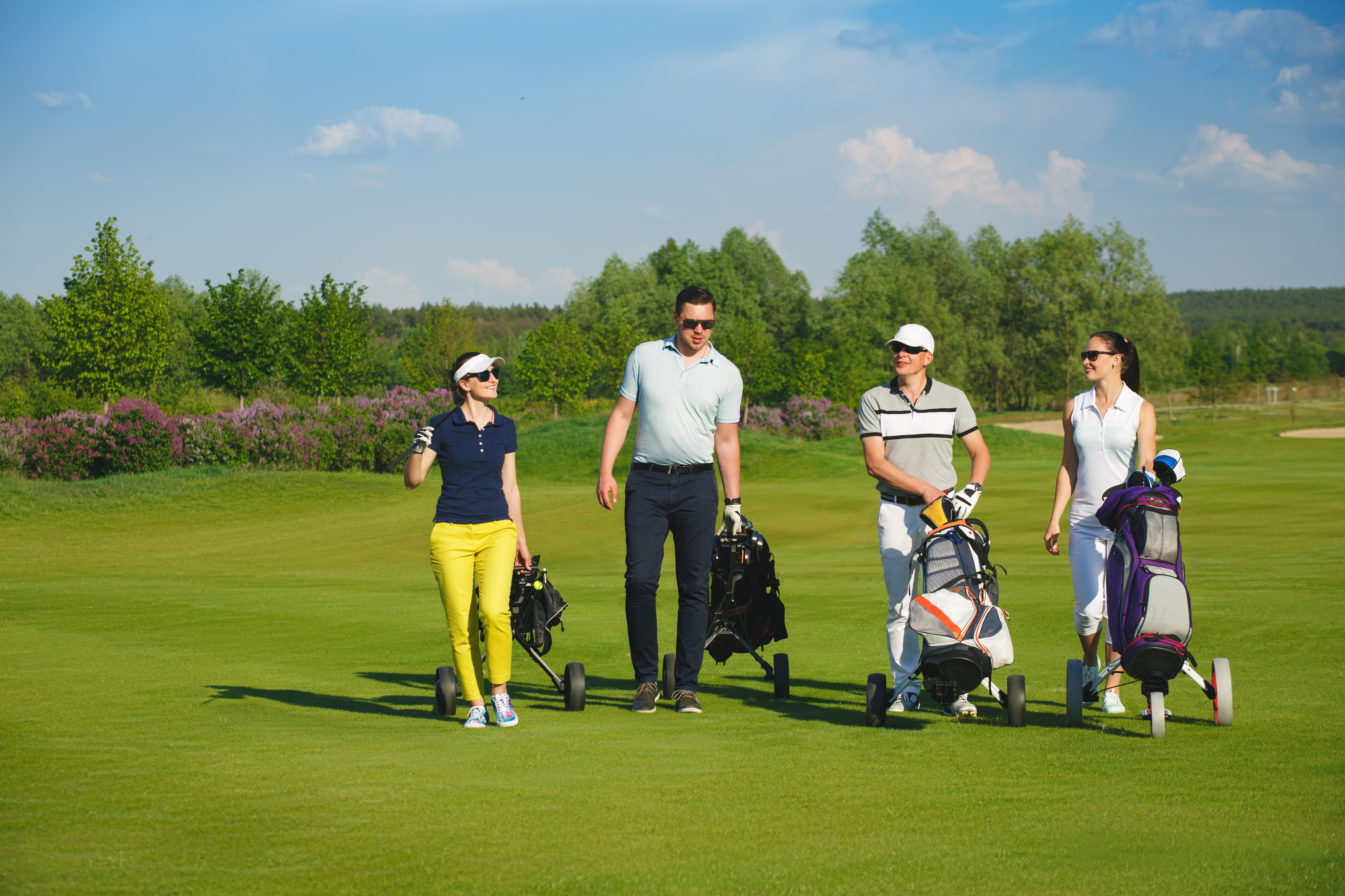 Four friends golfers walking on golf course at sunny day